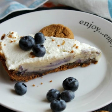 Creamy icebox pie on white plate with cookies and blueberries around it.