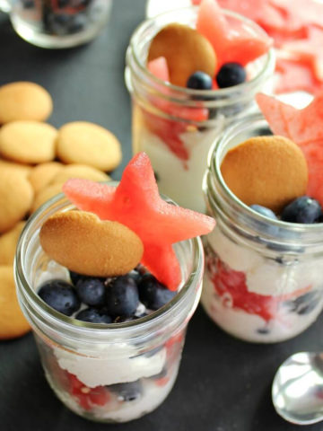 Glass mason jars with watermelon stars, cream, and blueberries.