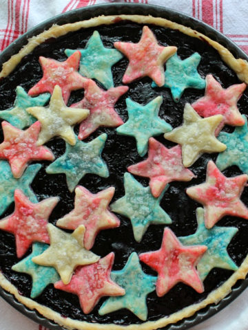Fruit tart with red and blue stars sitting on a gingham cloth.