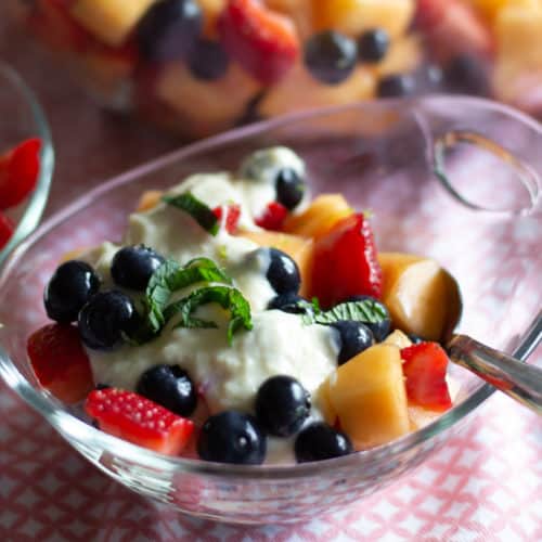 Bowl of fresh fruit salad with mint and cream.