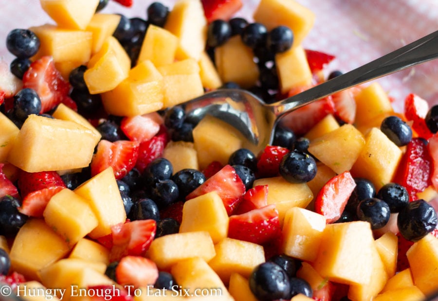 Sliced cantaloupe and strawberries tossed with blueberries in a clear bowl.