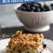 Slice of coffee cake with blueberries and a bowl of blueberries in background.