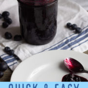 Jar of blueberry sauce on a white cloth.