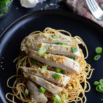 Vertical image of sesame noodles topped with sliced chicken.