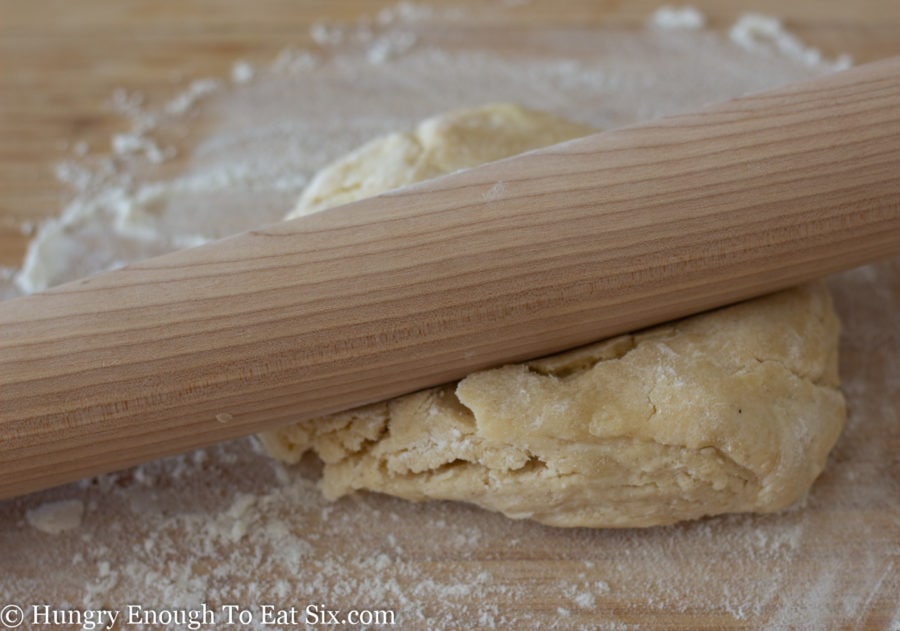 Mound of pie crust dough under rolling pin.