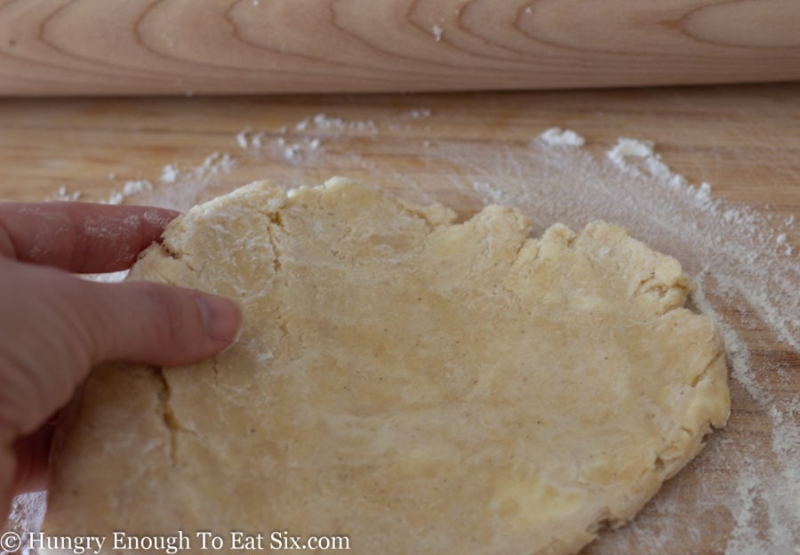 Hand moving dough next to a rolling pin.
