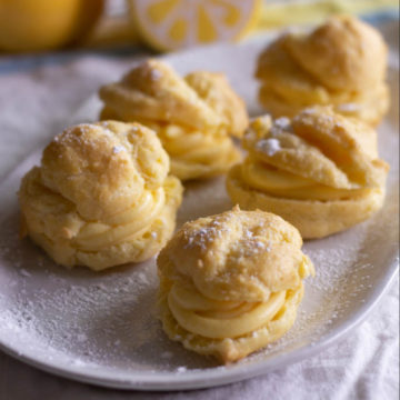 Cream puffs med gul sitron fylling på en hvit plate.