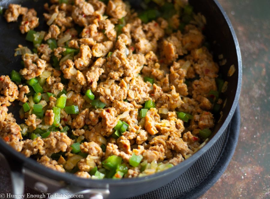 Cooked crumbled sausage with green peppers in a pan.