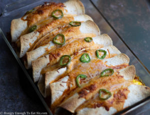 Pan of baked breakfast burritos with jalapenos on top.