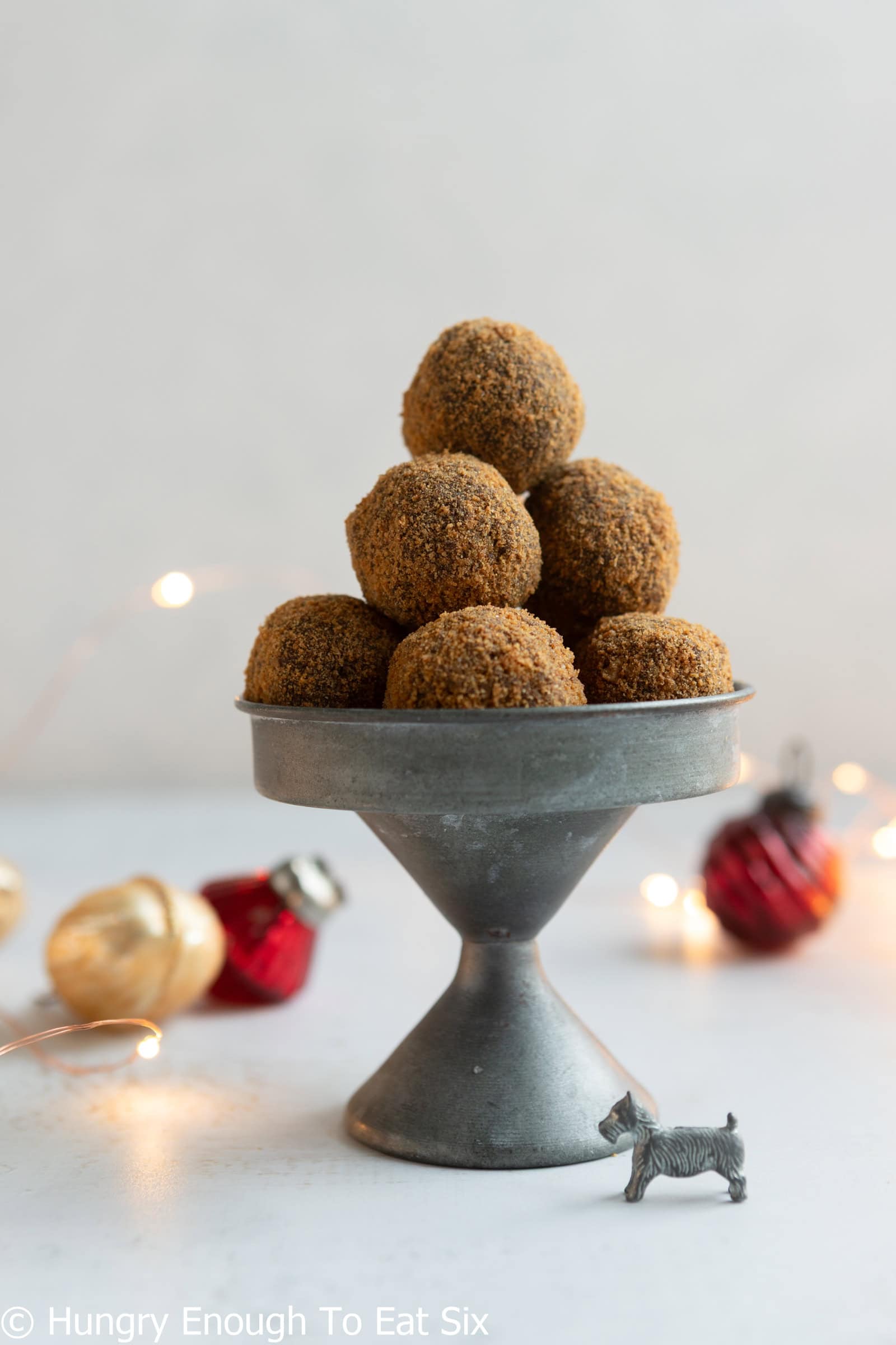 Tall dish with a pile of Ginger Cookie Chocolate Truffles and holiday ornaments in the background.