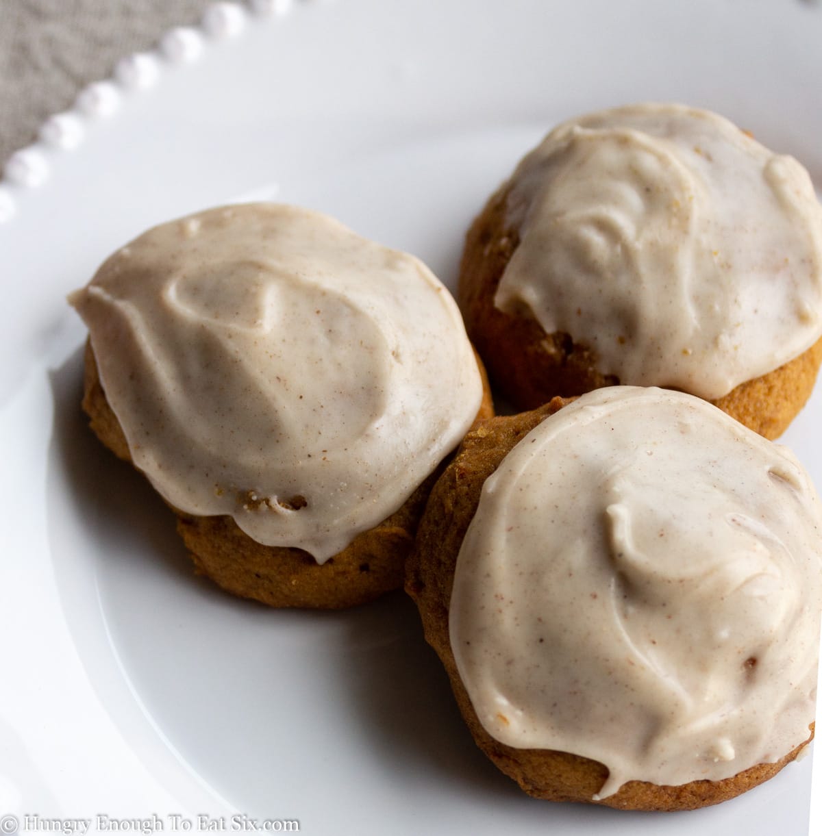 Pile of pumpkin cookies with frosting on a white plate