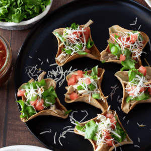 Chicken taco cups with toppings on a black dish.