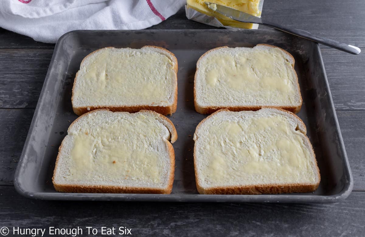 Four slices of buttered bread on a baking sheet.