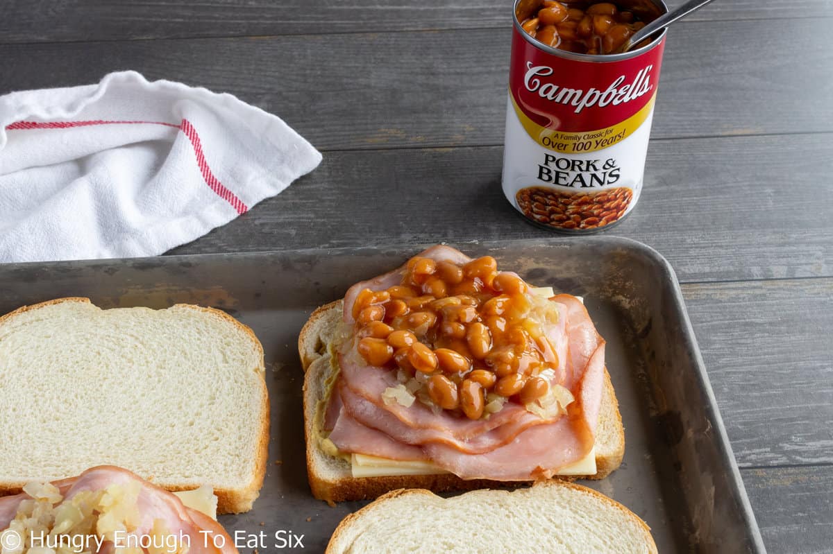 Sliced of bread with ham, cheese, and baked beans.