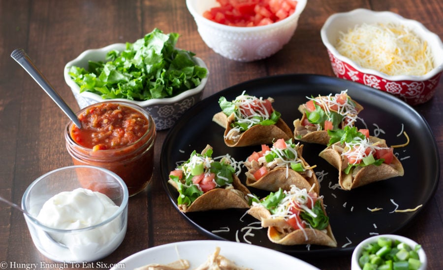 Filled taco cups surrounded by various taco toppings.