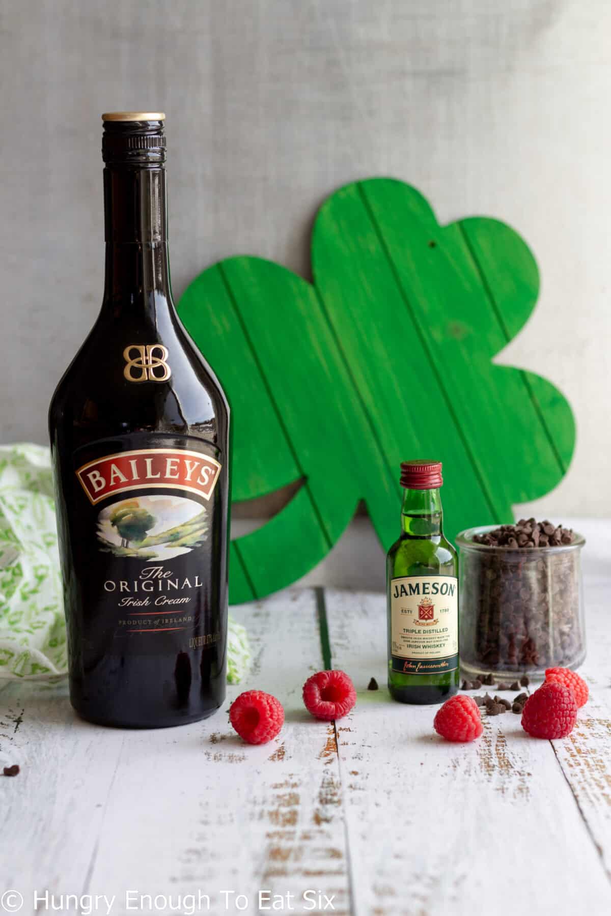 Bottle of Irish cream with whiskey bottle, chocolate chips, and raspberries.