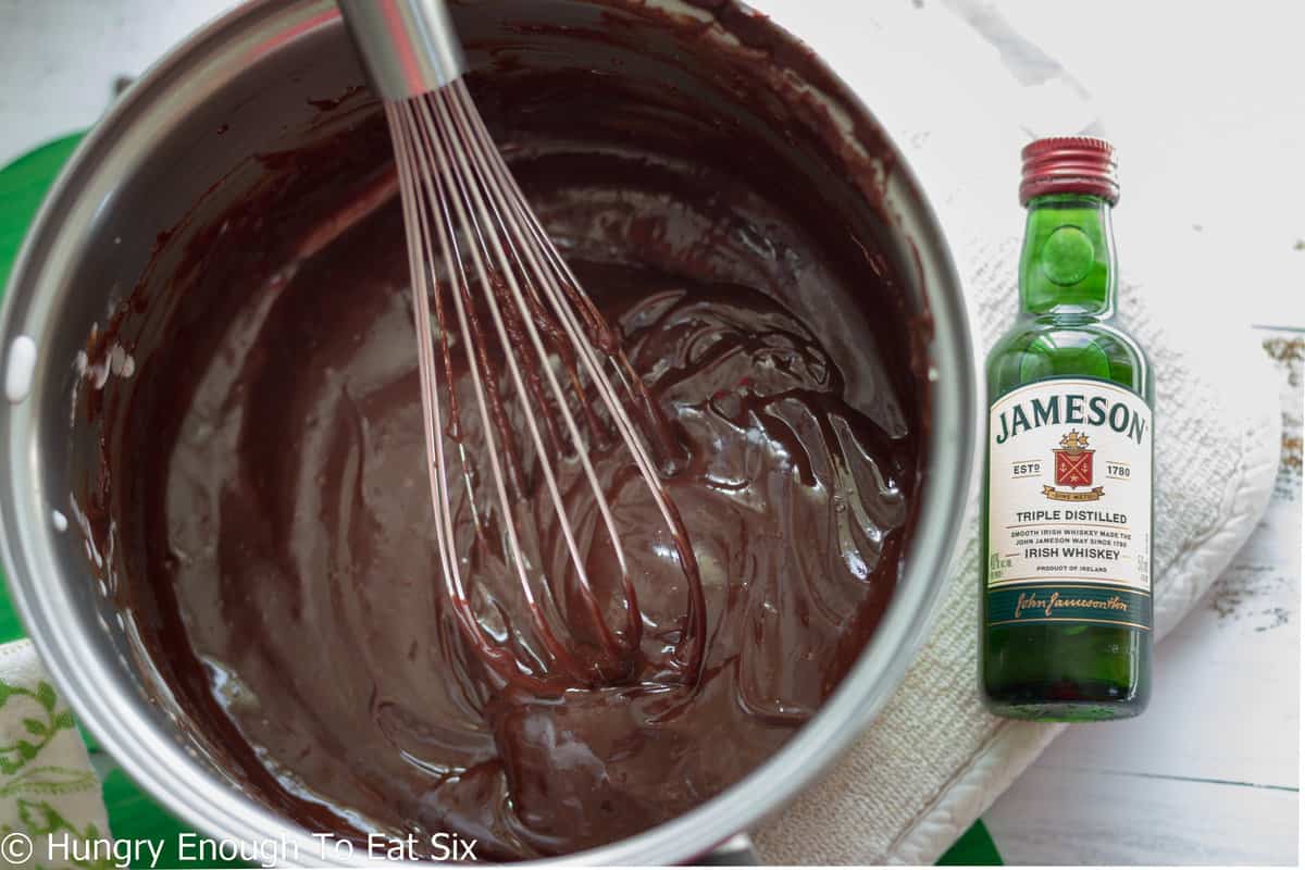 Chocolate sauce in pan next to bottle of whiskey.