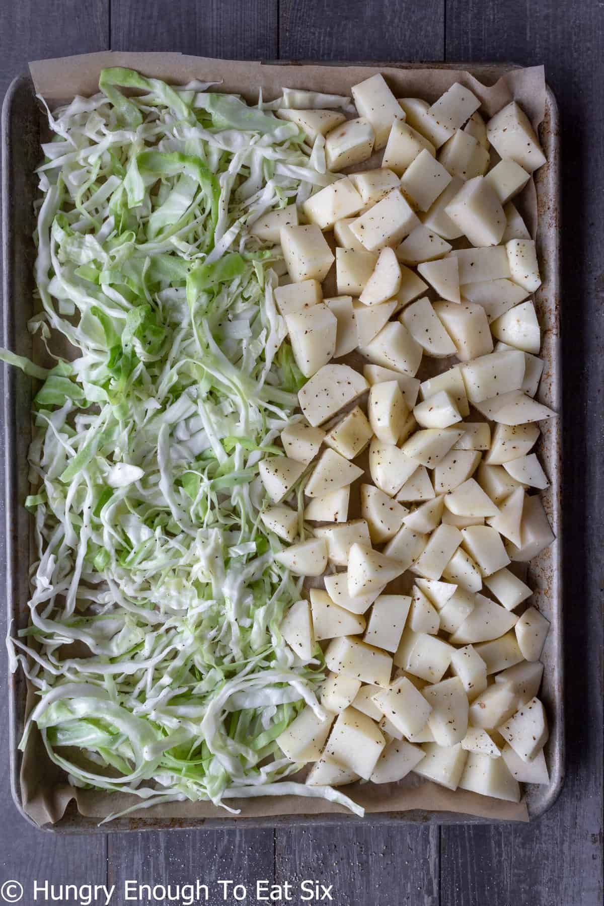 Uncooked sliced cabbage and potatoes on sheet pan.