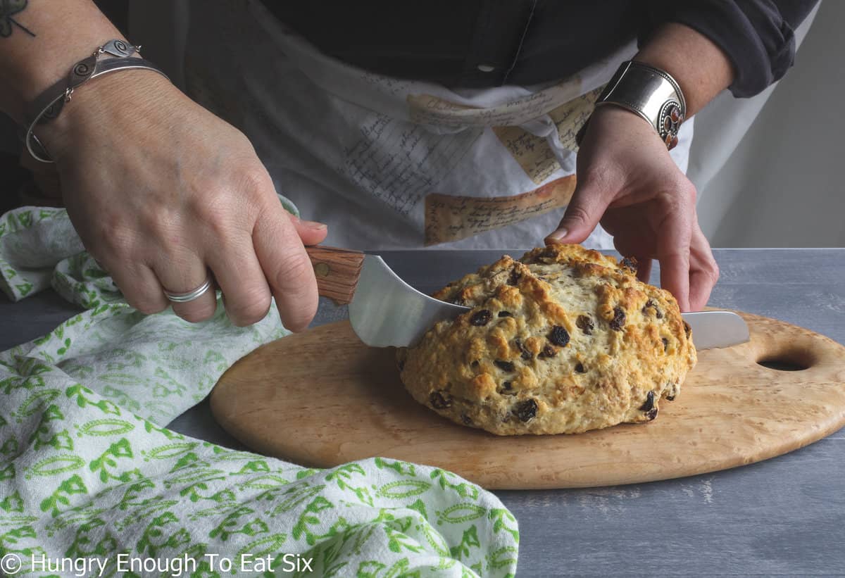 Hands holding and slicing a loaf of soda bread.