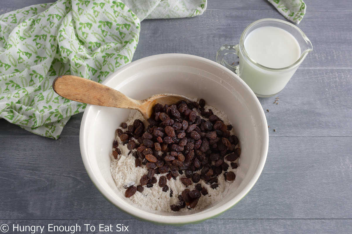 Raisins and flour in a mixing bowl with wood spoon.