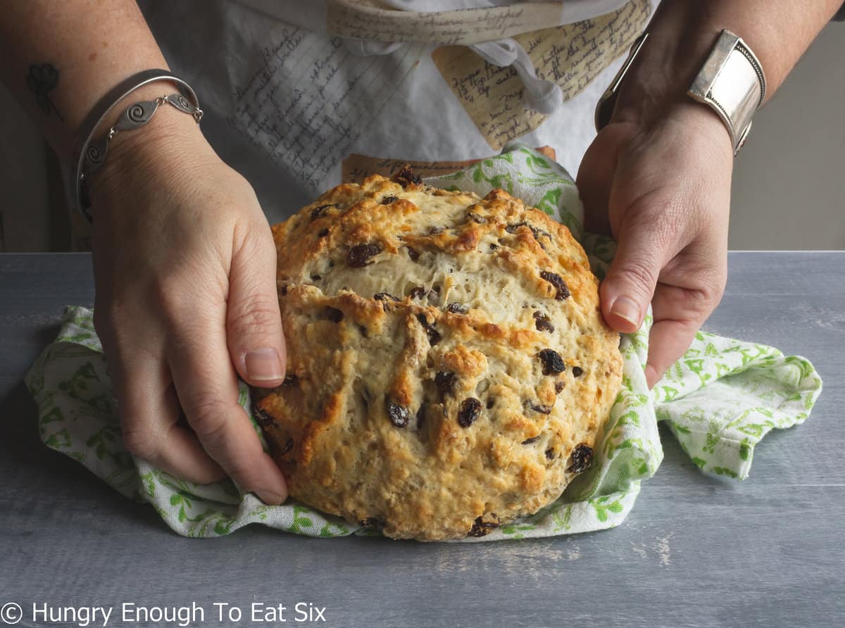 Hands holding a round loaf of soda bread.