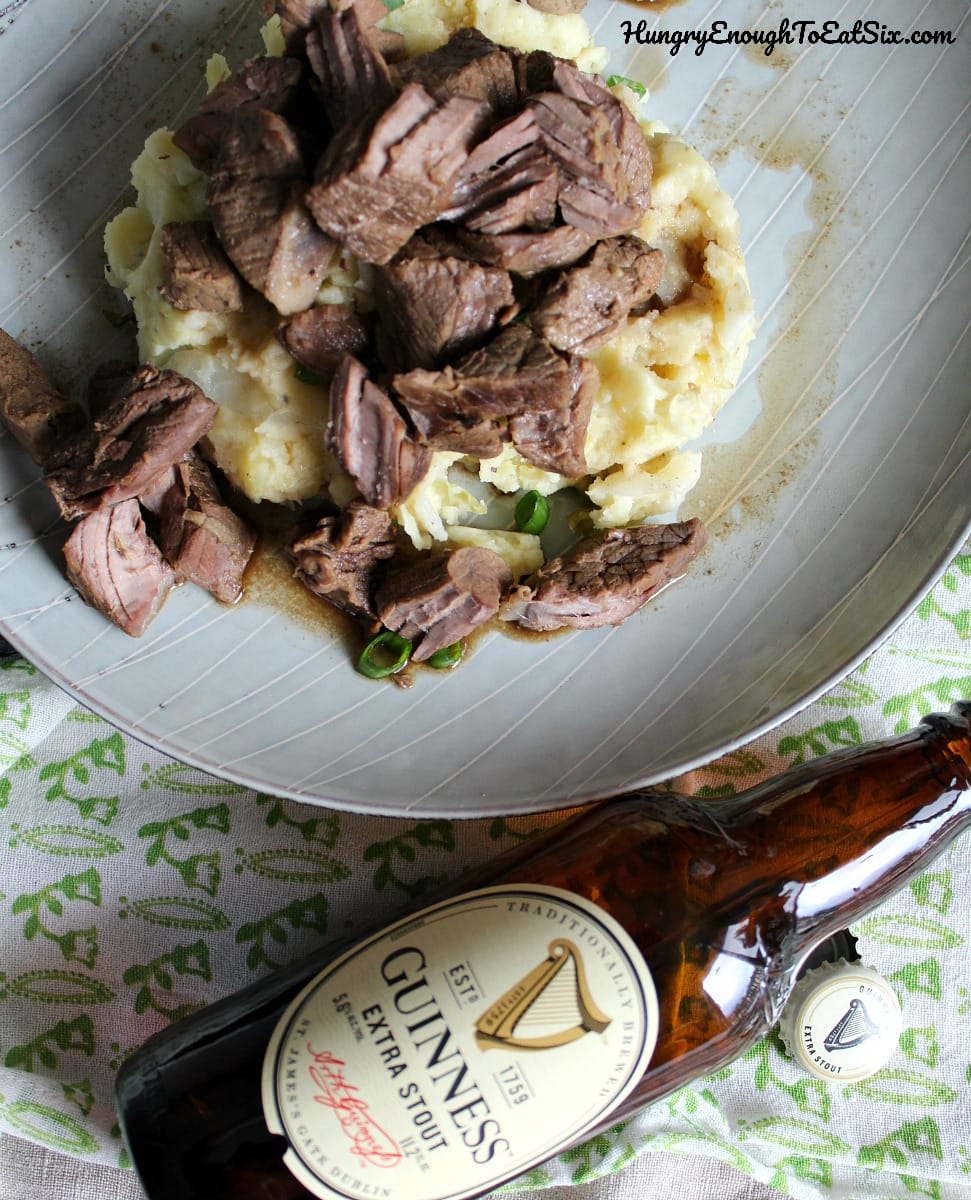 Plate of beef and potatoes next to a bottle of beer