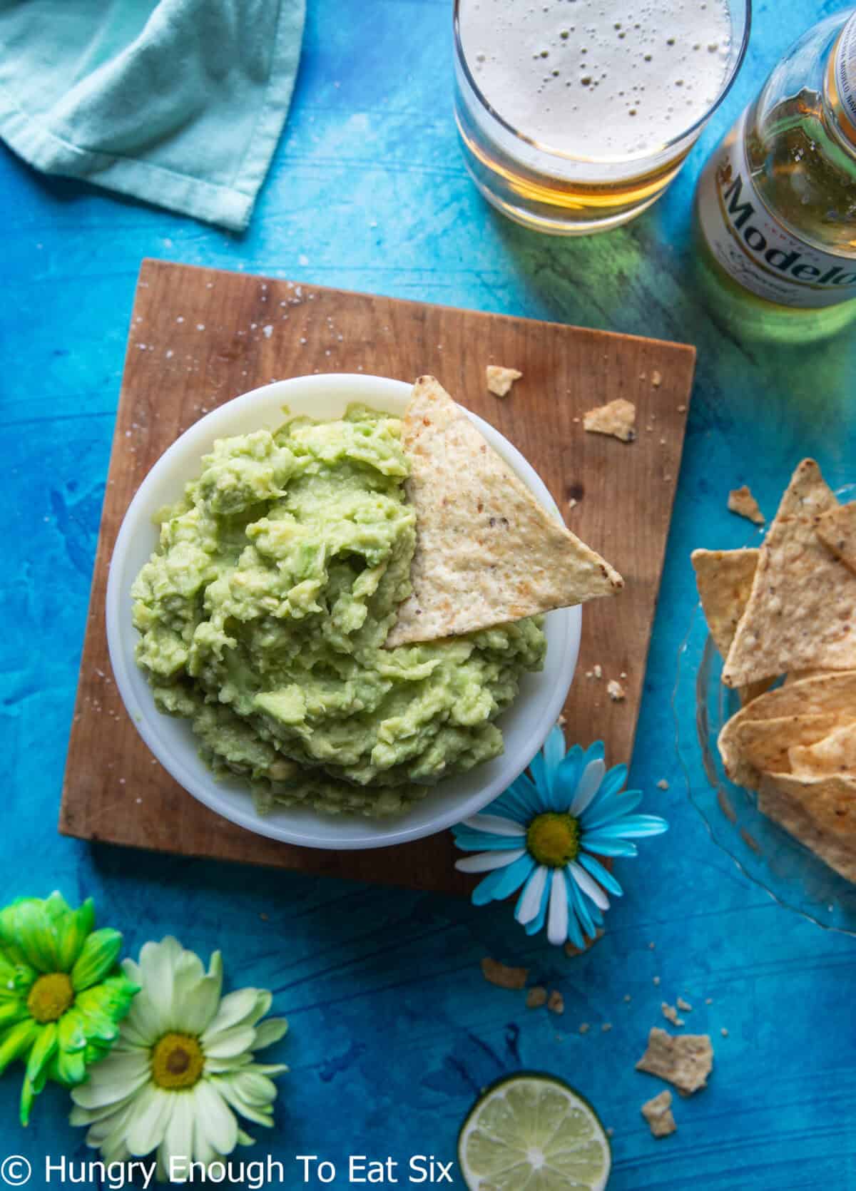 Bowl of guacamole on a table with limes and a beer.
