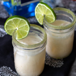 Coconut and lime margaritas in small mason jars with limes.