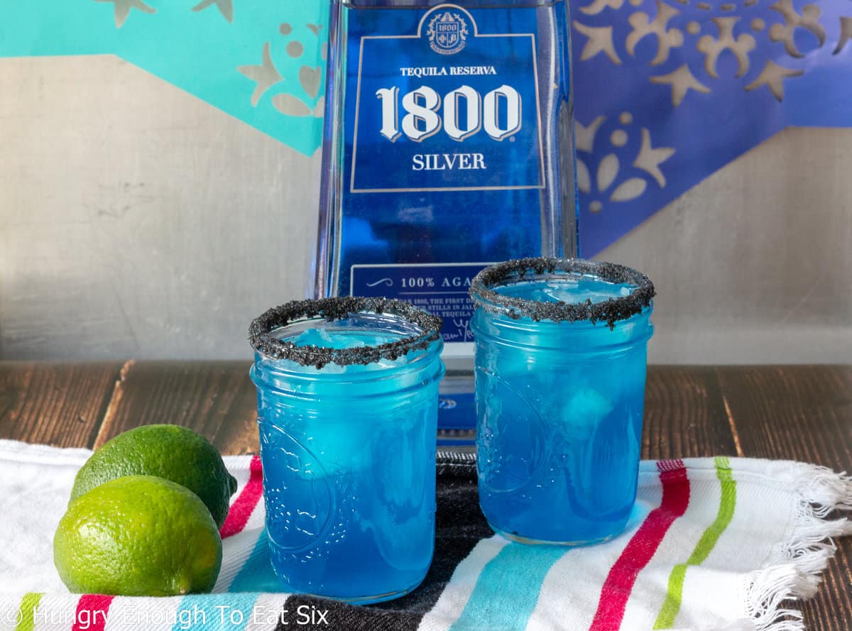 Blue margaritas in front of tequila bottle.