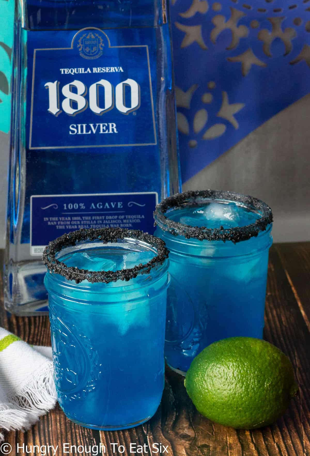 Blue margaritas with black rims and lime in front.