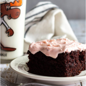 Slice of chocolate cake with strawberry frosting next to a glass of cold milk.