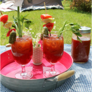 Bloody Marys on a pink tray in front of a campsite.