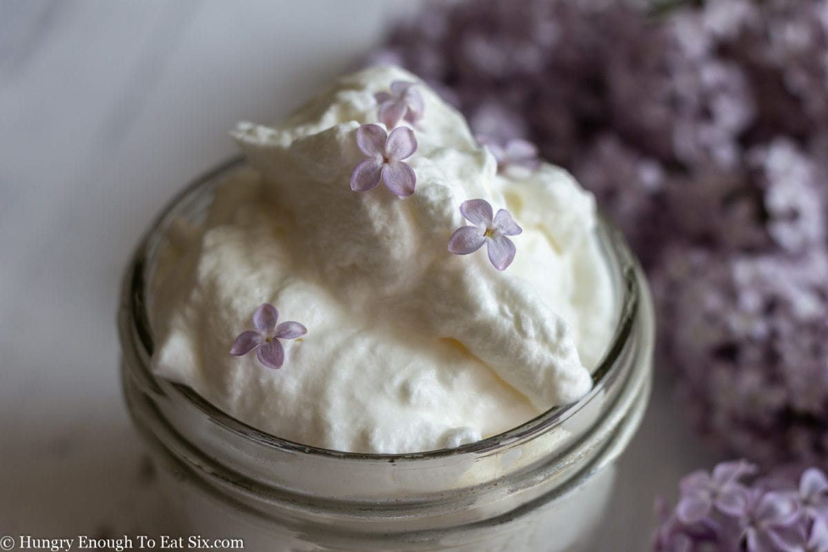 Whipped cream with lilac flowers on top and in background.