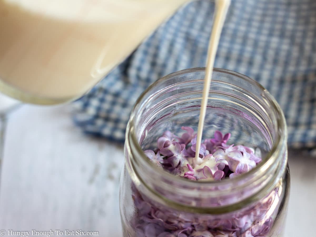 Glass jar with lilac blooms inside and cream being poured in.