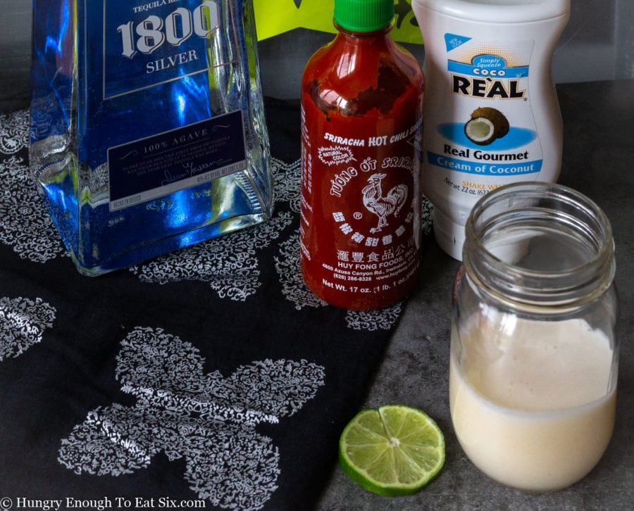Ingredients for a margarita including sriracha, tequila, and cream of coconut.
