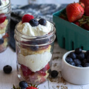 White wood surface with berries and a mason jar with layered cream and fruit