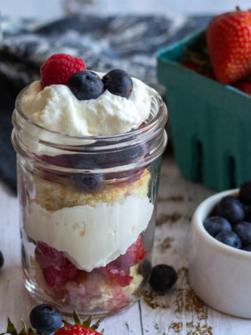 White wood surface with berries and a mason jar with layered cream and fruit