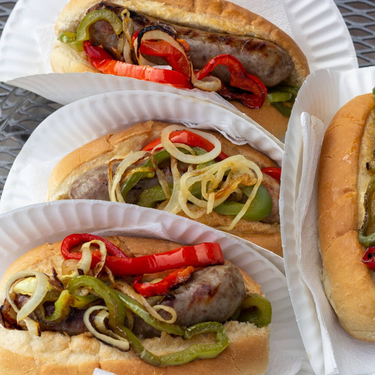 Four Buns holding sausage and grilled peppers and onions.