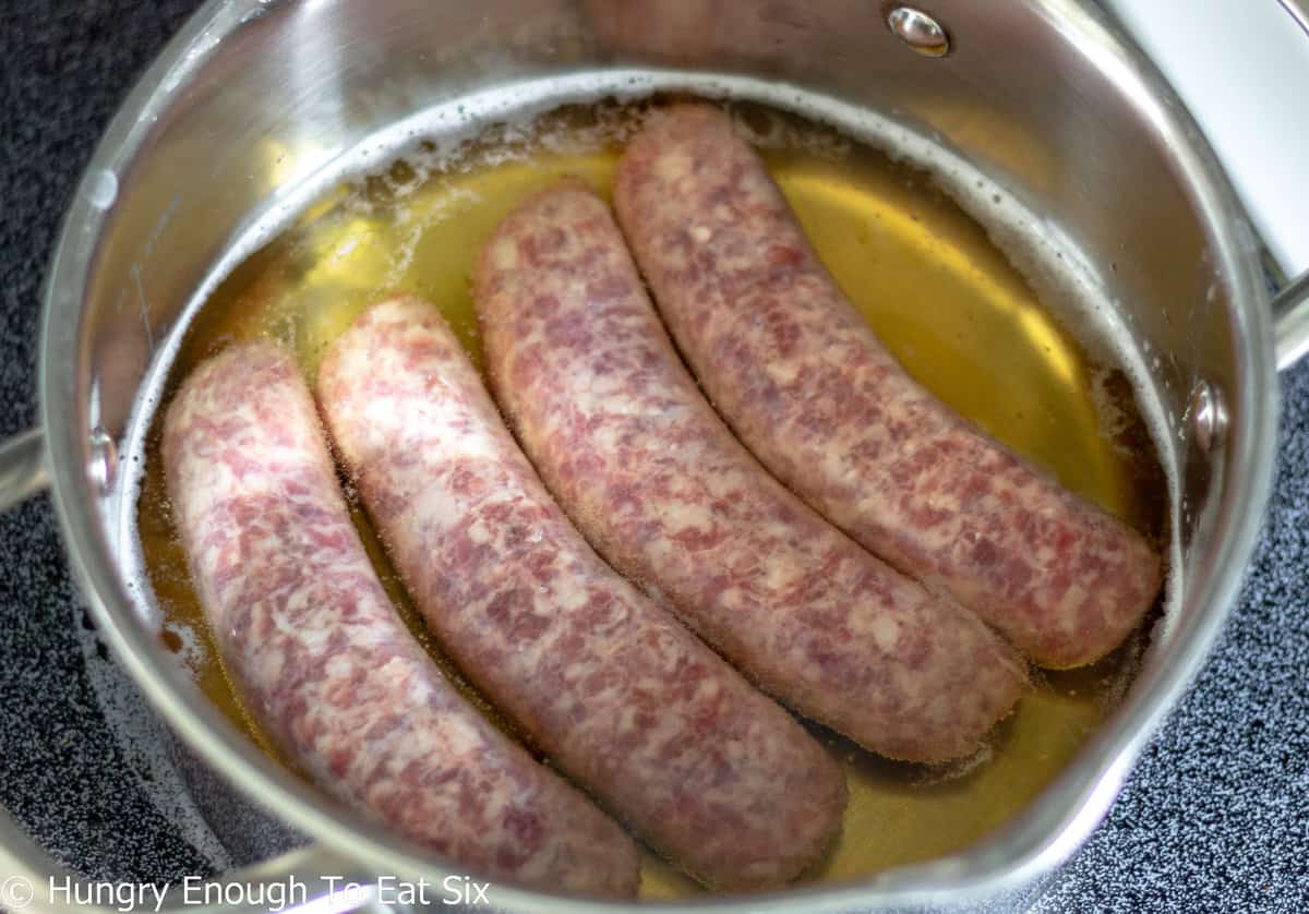 Four sausages in beer in a saucepan.