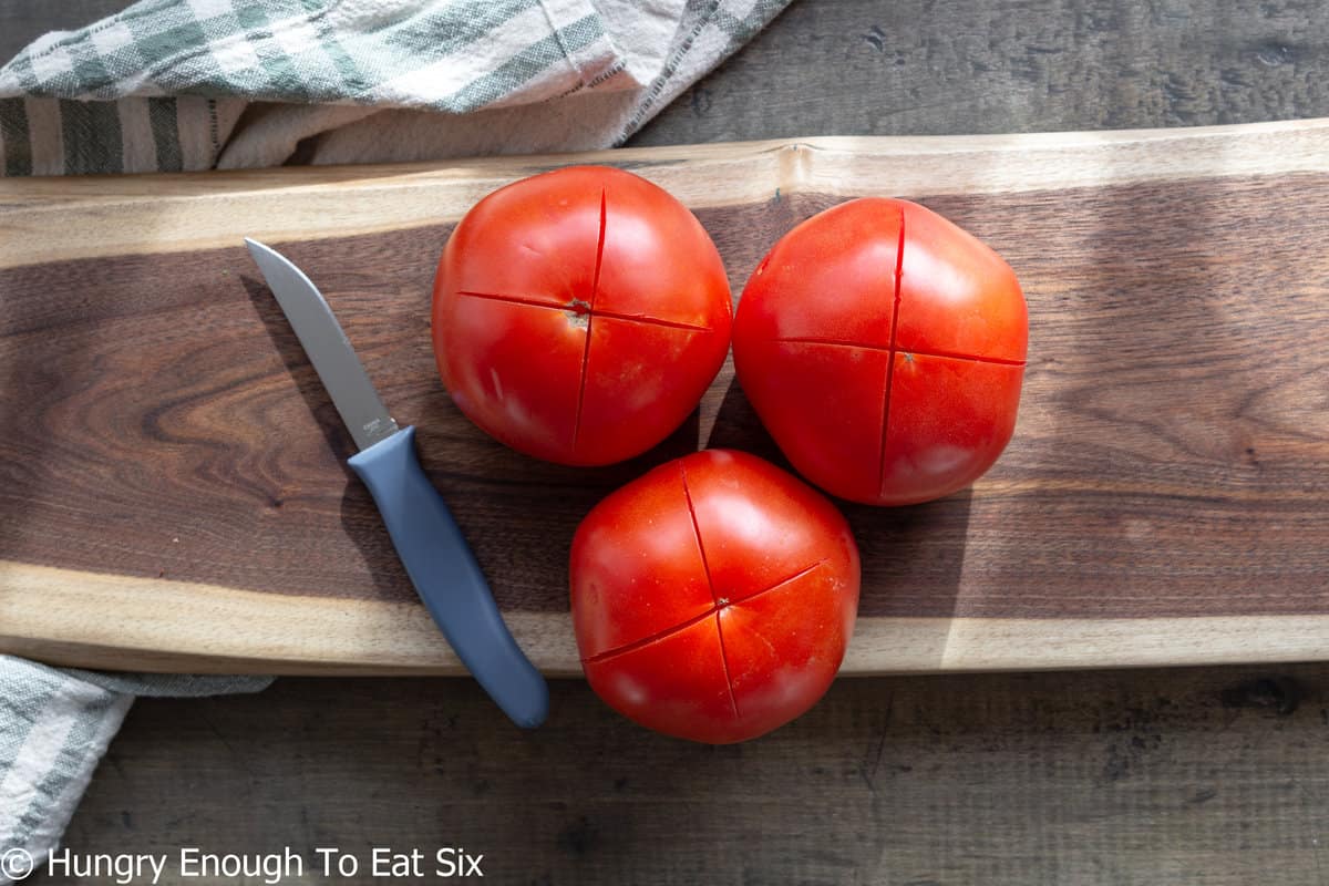 Three tomatoes on cutting board with x-sliced bottoms.