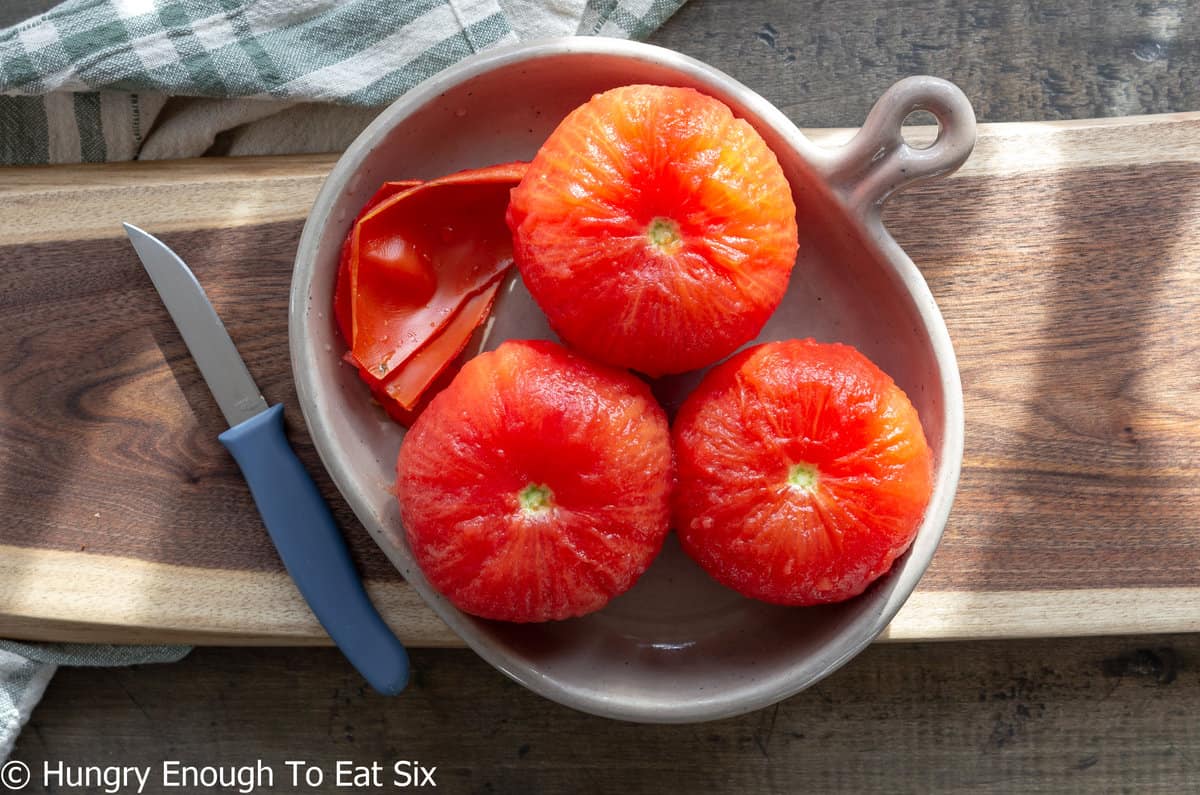 Three whole peeled tomatoes on a plate.