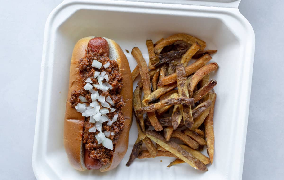 Hot dog in bun with meat sauce and chopped onion, with side of fries.