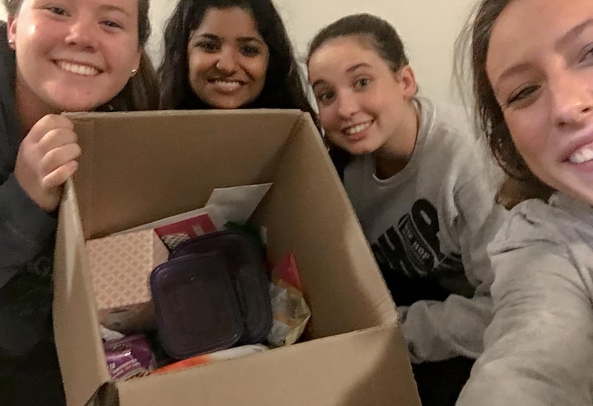 Four college-aged women with box of treats.