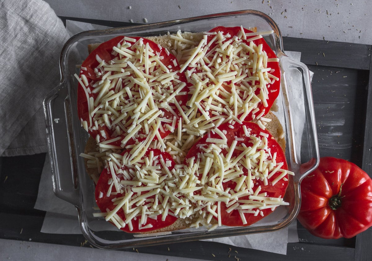 tomato slices topped with shredded cheese in a pan