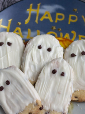 White chocolate ghost cookies laying on a Halloween decorative plate