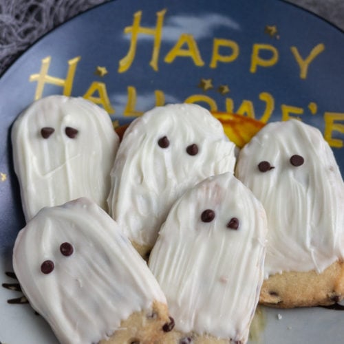 White chocolate ghost cookies laying on a Halloween decorative plate