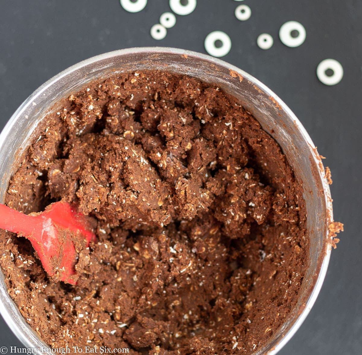 Chocolate oat cookie dough in a metal mixing bowl with a red spatula