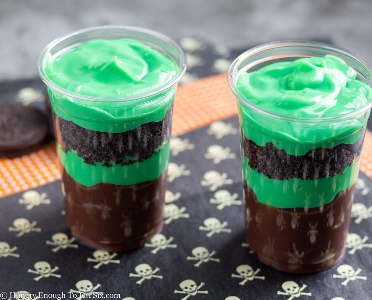 Two plastic cups holding greenand brown layered dessert