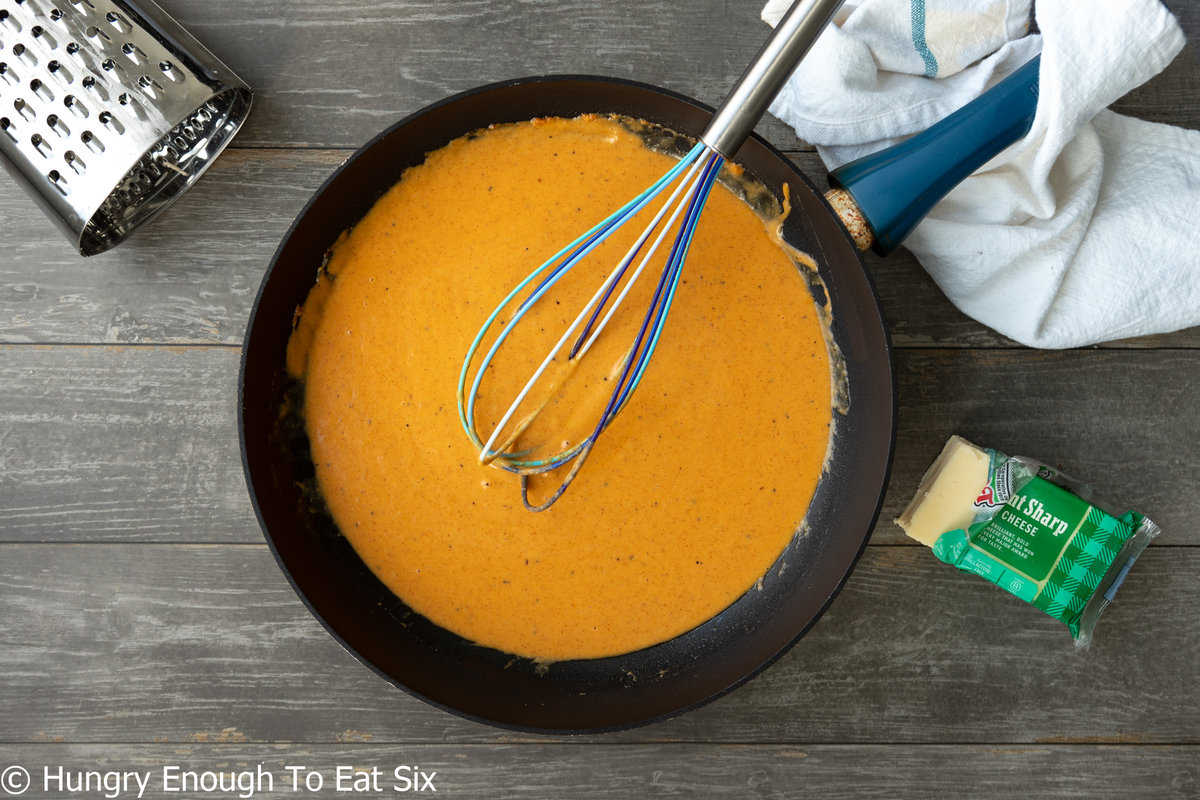 Black skillet with orange cheese sauce and whisk.