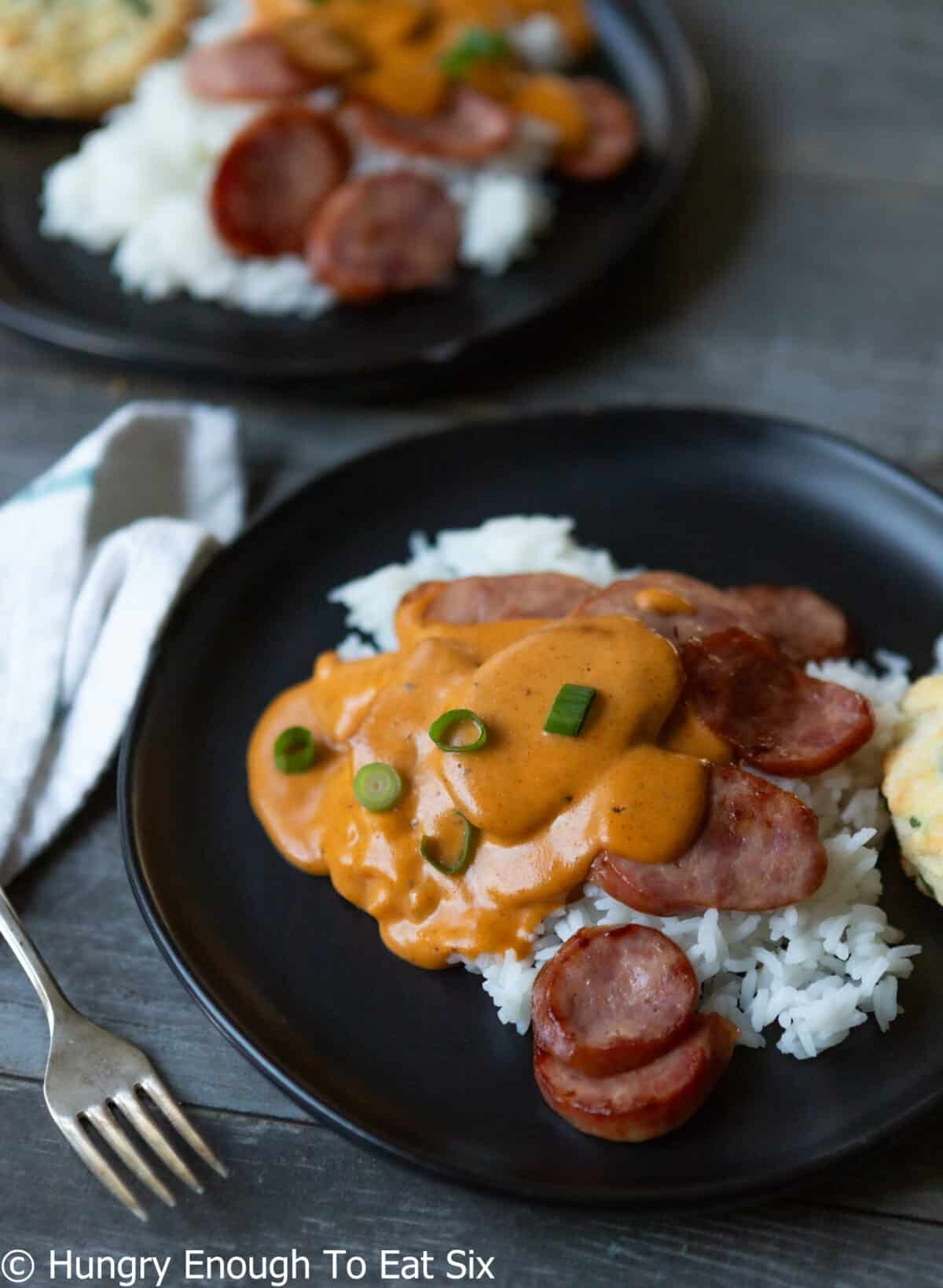 Black plate with rice, sausage, and cheese sauce.